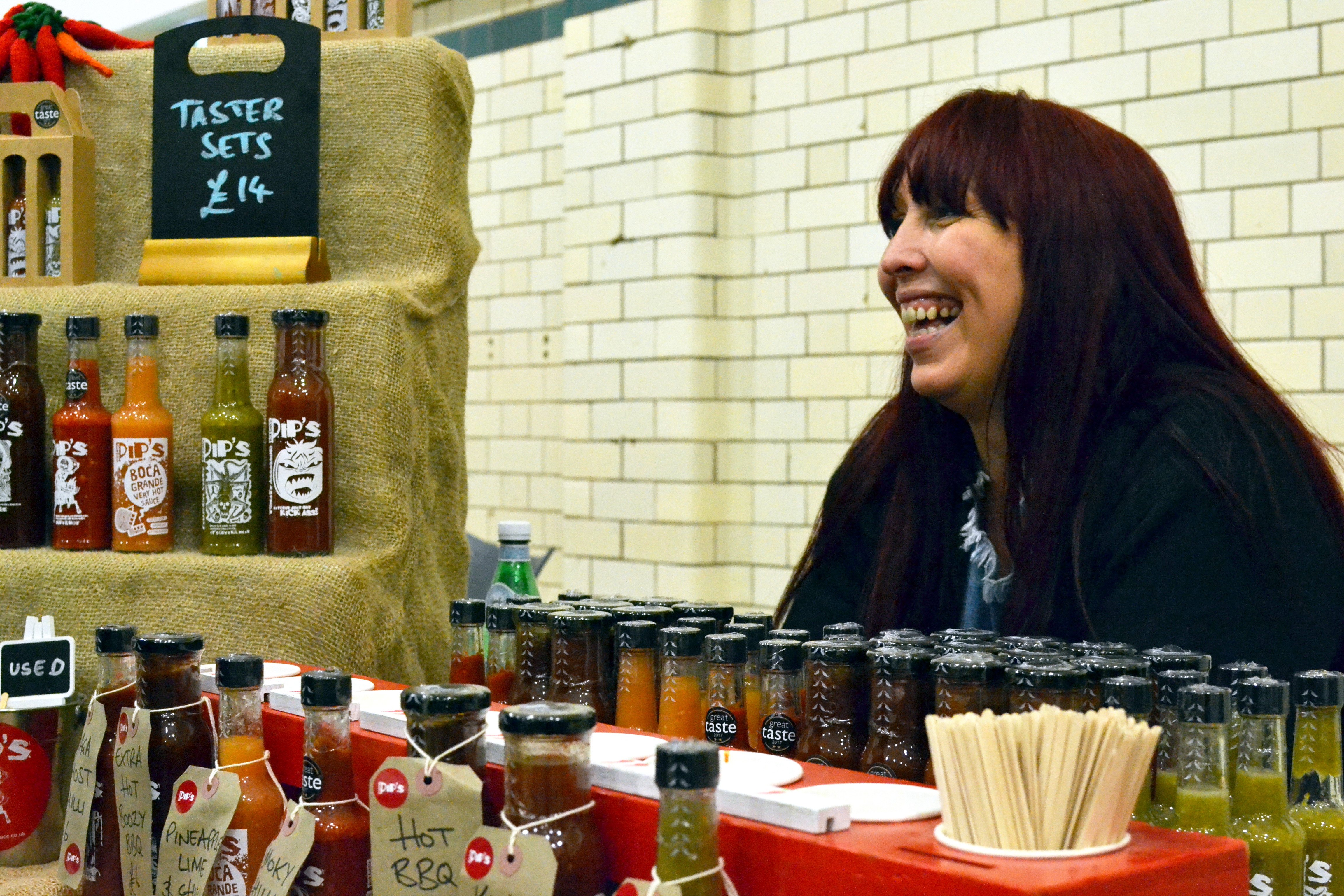 Pip sitting smiling from behind her Hot Sauce bottles