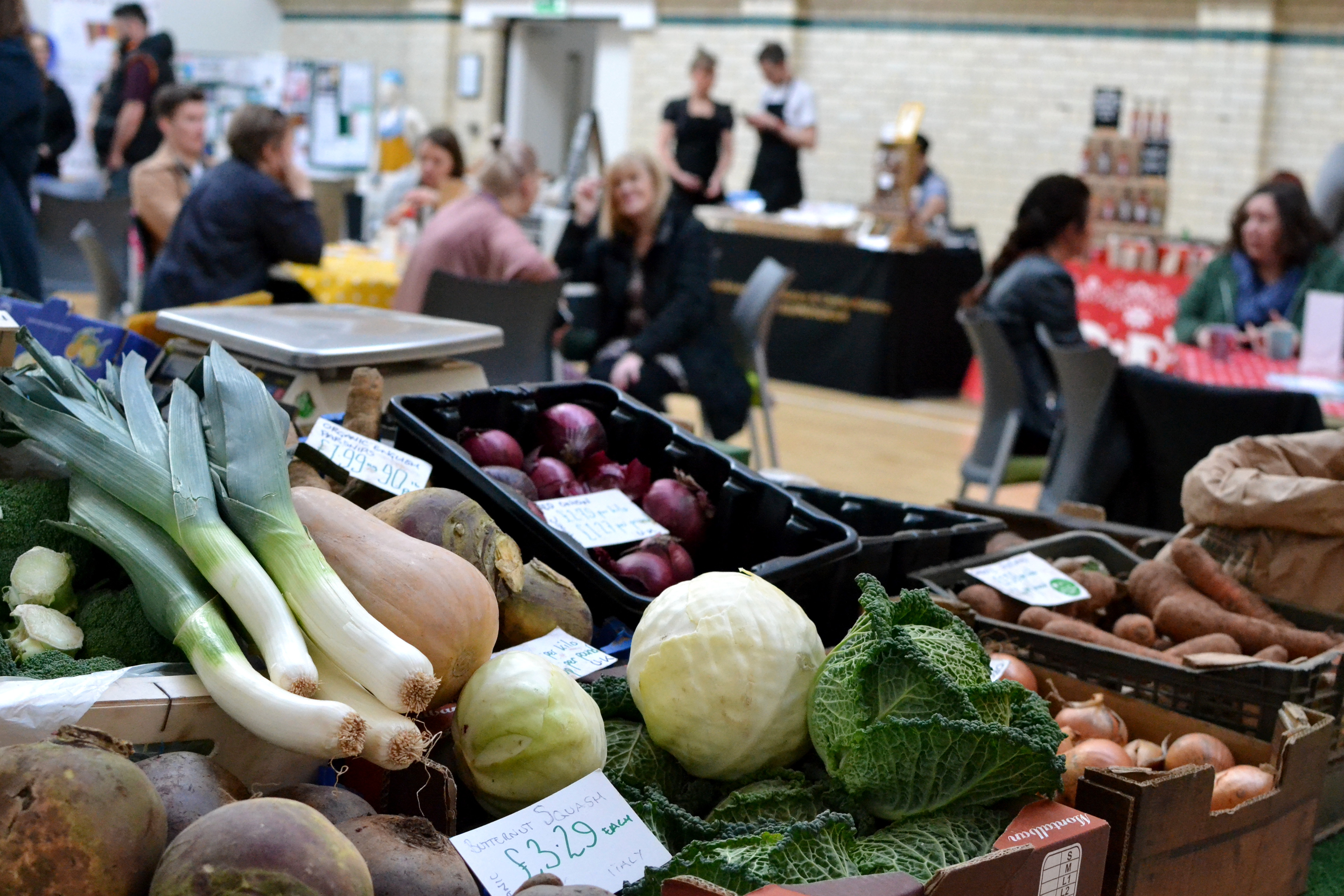 A stall serving fresh veg with Market customers in the hall behind